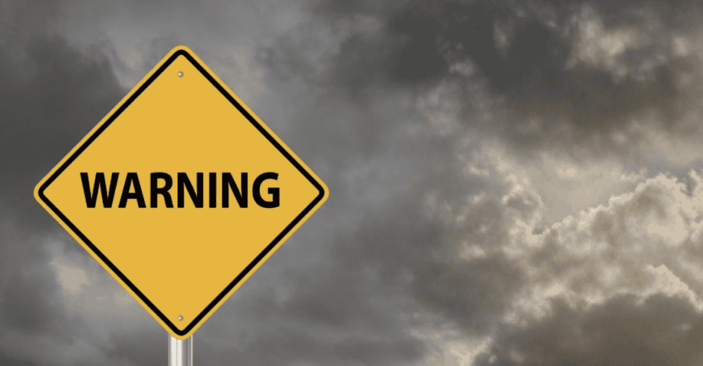 A yellow warning sign with the word WARNING in black letters stands in front of a cloudy, dark sky, suggesting a potential danger or alert.