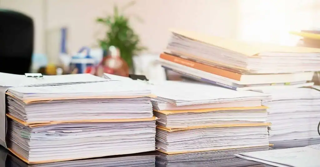 Tall stacks of unpaid account files and paperwork piled on an office desk